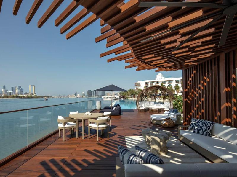 Moderní hotelová terasa se sezením s výhledem na vodu a město.