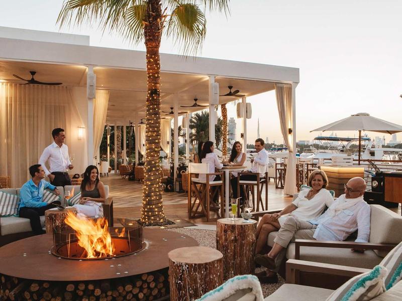 Pohodlná venkovní terasa hotelu s hosty a ohništěm uprostřed.