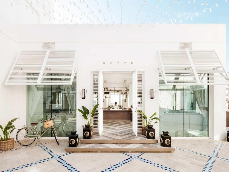 Jasný, moderní vstup do hotelu se skleněnou fasádou a rostlinami.