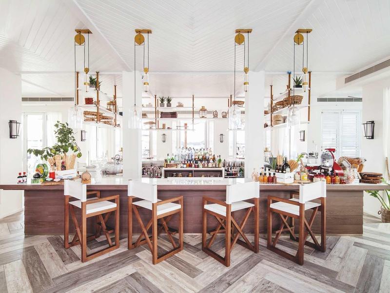 Moderně zařízený bar s dřevěnými židličkami a bílými zdmi v jasném hotelovém prostředí