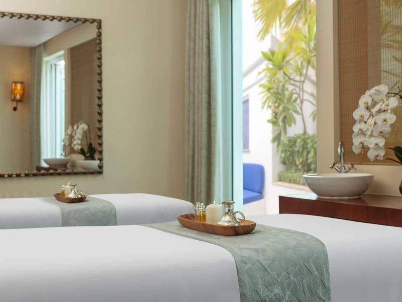 Příjemná léčebná místnost se dvěma masážními stoly, okno se zelenými závěsy a dekoracemi.