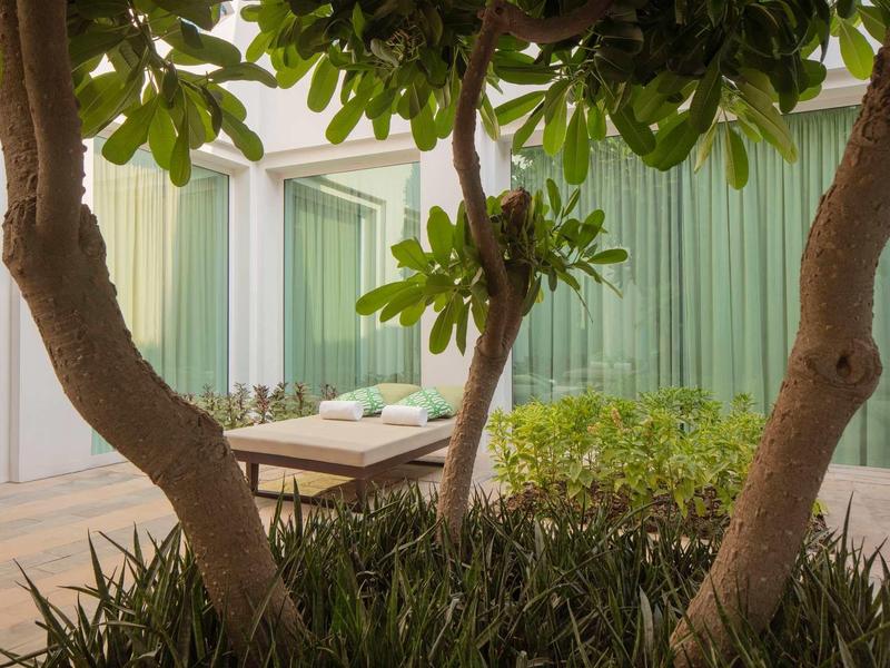 Moderní venkovní prostor se zelenými rostlinami, stoly a sezením vedle budovy.