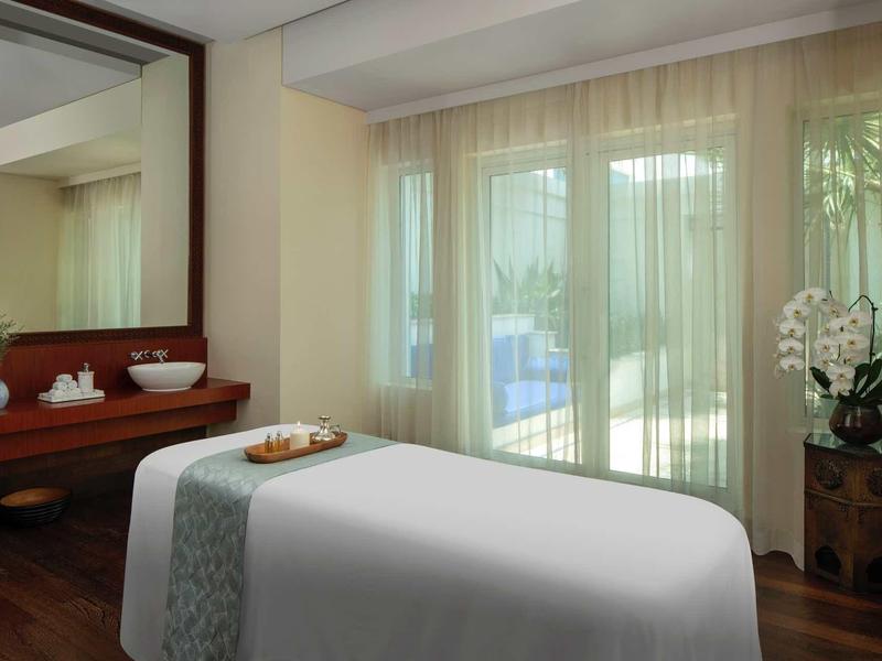 Světelná wellness místnost s masážním stolem a výhledem na terasu se zahradou.