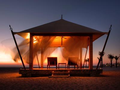 Gemütlicher Massageraum mit zwei blauen Behandlungsbetten, Fenster und Holzwänden, ruhige Atmosphäre.