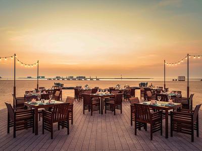 Außenbereich eines Hotels mit gedeckten Tischen und Sonnenuntergang am Meer im Hintergrund.
