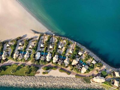 Luftaufnahme einer Küstenresidenz mit Häusern, Gärten und Strand an türkisblauem Wasser.