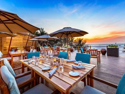 Terrasse eines Hotels mit gedeckten Tischen und Blick auf den Sonnenuntergang über dem Meer.