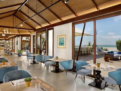 Modernes Restaurant mit blauen Stühlen und großer Glasfront mit Blick auf das Meer.