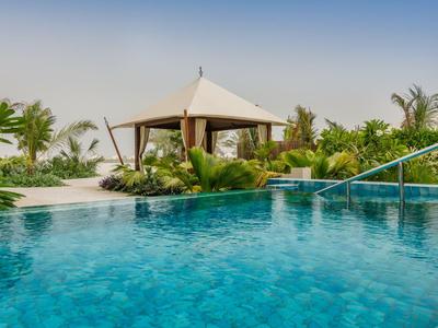 Schwimmbad mit klarem blauem Wasser, Palmen und einem Zeltdachpavillon im Hintergrund.