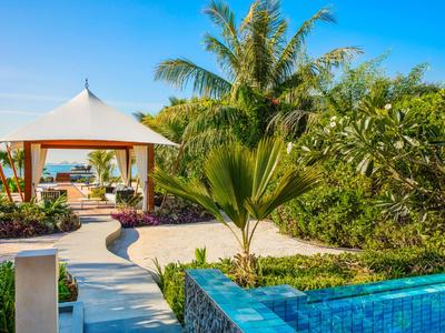 Hotelpool mit blauem Wasser, Palmen und weißem Pavillon bei sonnigem Himmel.