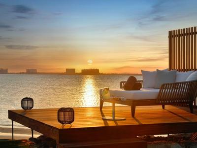 Sonnenuntergang über Wasser mit Holzterrasse und Sitzbank im Vordergrund.