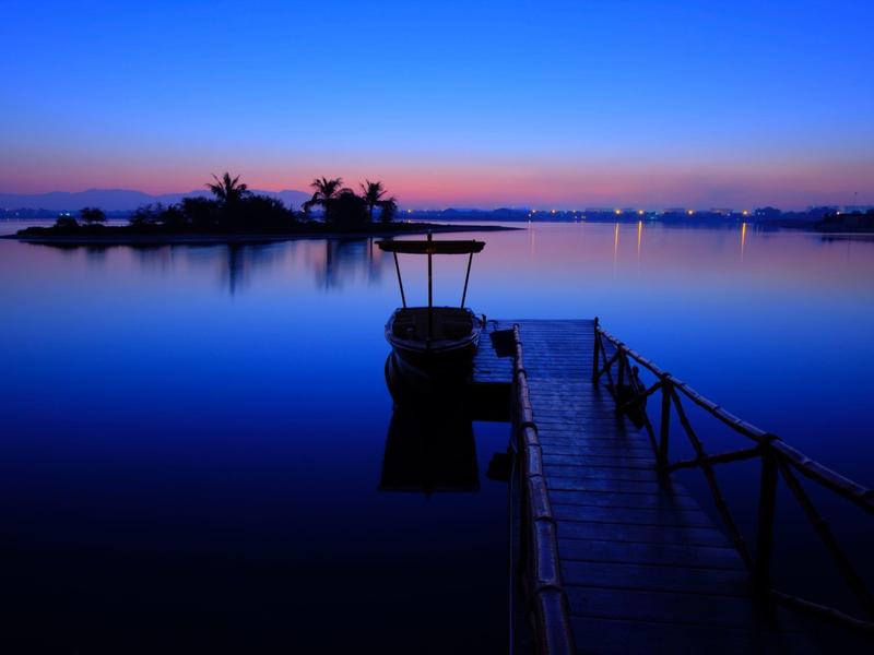 Ein Steg führt zu einem kleinen Boot bei ruhigem Wasser während der Dämmerung.