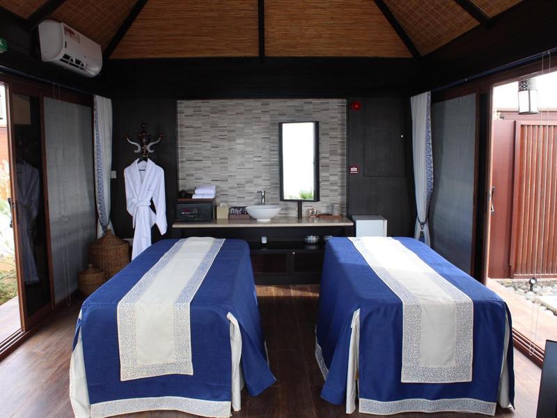 Gemütlicher Massageraum mit zwei blauen Behandlungsbetten, Fenster und Holzwänden, ruhige Atmosphäre.