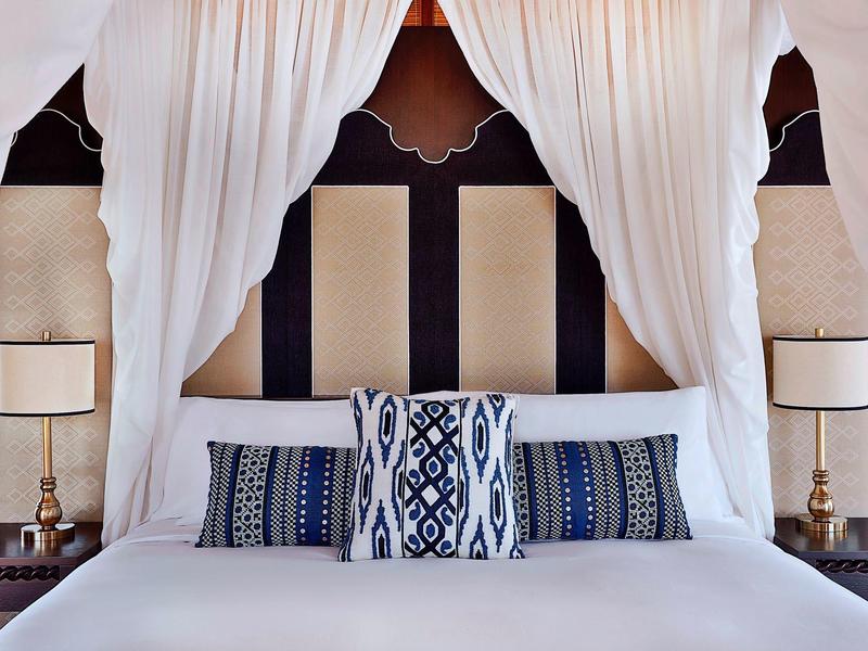 Elegantes Doppelbett mit weißen Vorhängen und dekorativen Kissen in einem stilvollen Hotelzimmer.