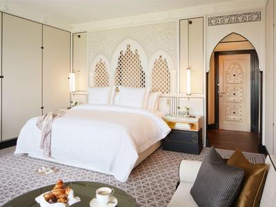 Elegantní ložnice s bílou postelí, dekorativními stěnovými prvky a útulným posezením.