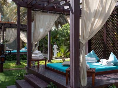 Pohodlná krytá lehátka s bílými závěsy a modrými polštáři v tropické zahradě.