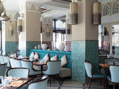 Světle zařízená hotelová restaurace s moderními židlemi a tyrkysovými kachličkami.