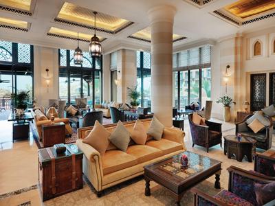 Lounge de hotel luminosa con áreas de descanso, cojines y grandes ventanas con vista al exterior.