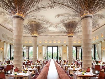 Restaurante elegante con columnas en forma de palma y mesas elegantemente preparadas.