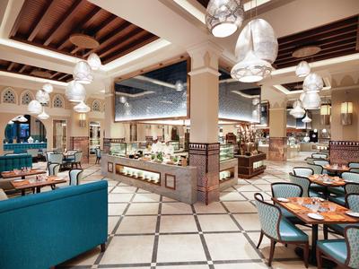 Prostorná hotelová jídelna s modrými židlemi, dřevěnými stolky a moderními stropními svítidly.