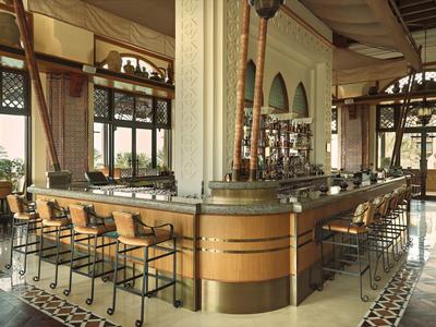 Elegantní hotelový bar s dřevěným pultem, stoličkami a velkými okny s výhledem ven.