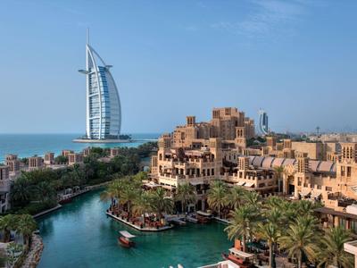 Luxuriöse Hotelanlage mit traditionellen Gebäuden und Wasserwegen, im Hintergrund markantes Segelhaus am Meer.
