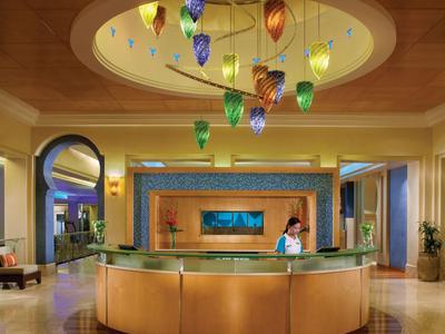 Recepción de hotel elegante con mostrador redondo y lámparas colgantes coloridas bajo un techo circular.