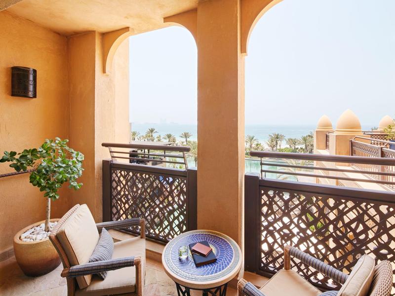 Balkon se dvěma křesly, malým stolem, rostlinou a výhledem na moře za slunného počasí.