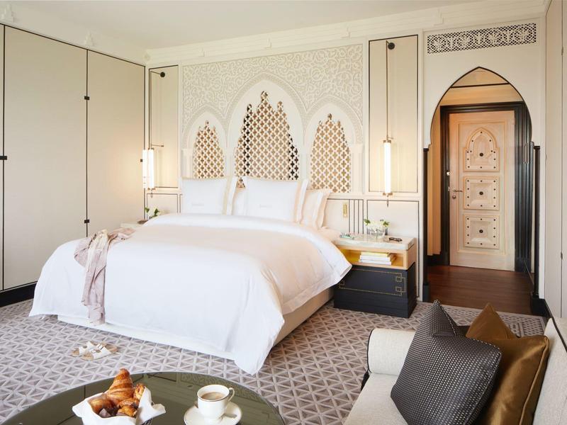 Elegantní ložnice s bílou postelí, dekorativními stěnovými prvky a útulným posezením.