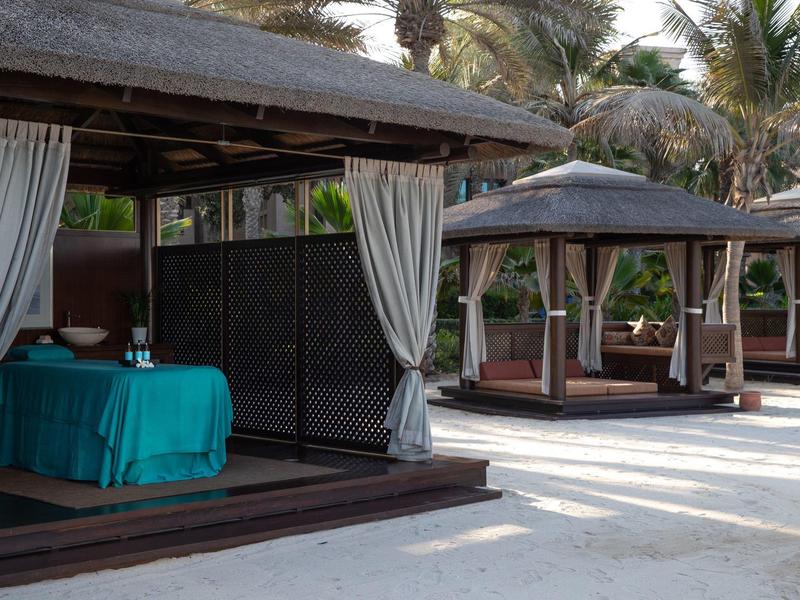 Plážová oblast s krytými lehátky a masážním stolem pod palmami.