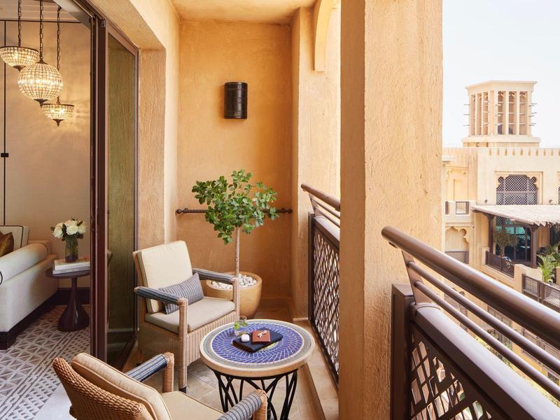 Balkon s křesly, stolem a rostlinami v hotelu s výhledem na tradiční budovy.