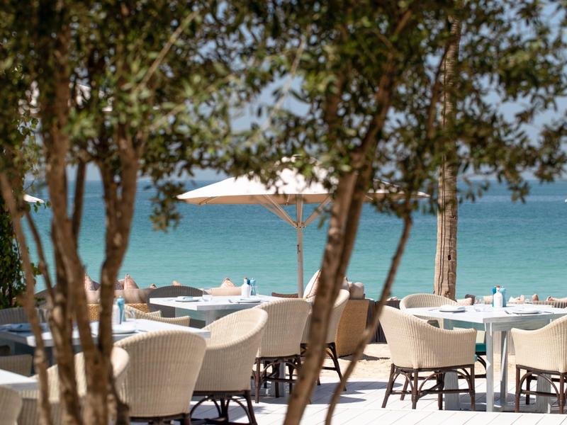 Venkovní posezení plážové restaurace s stoly, židlemi a výhledem na moře.