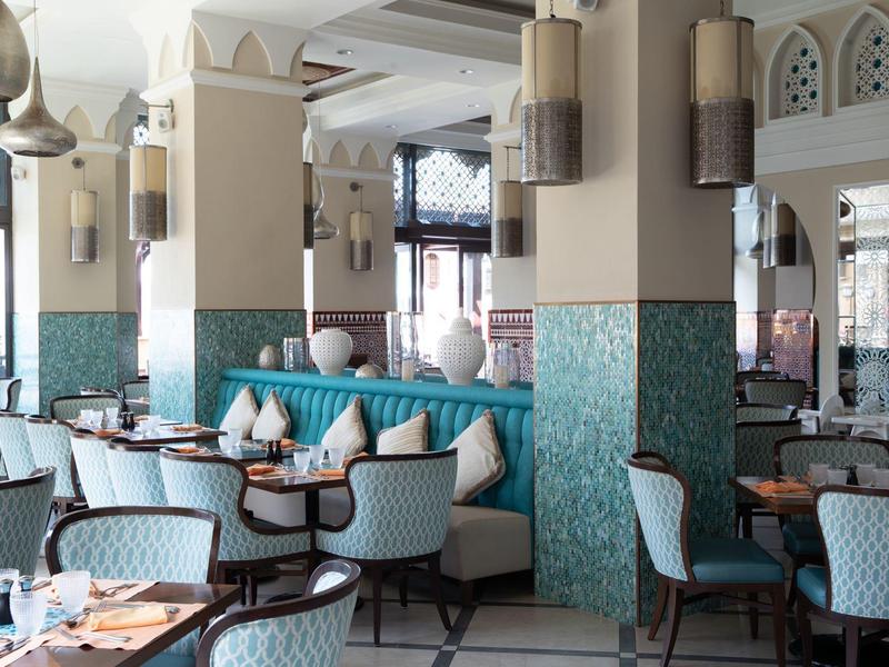 Světle zařízená hotelová restaurace s moderními židlemi a tyrkysovými kachličkami.