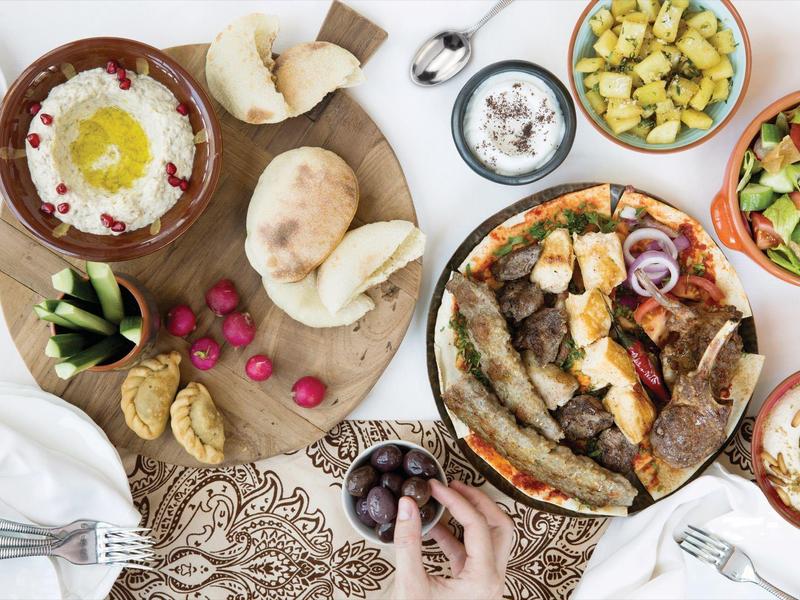 Různé středomořské pokrmy na stole, včetně zeleniny, chleba a dipů.