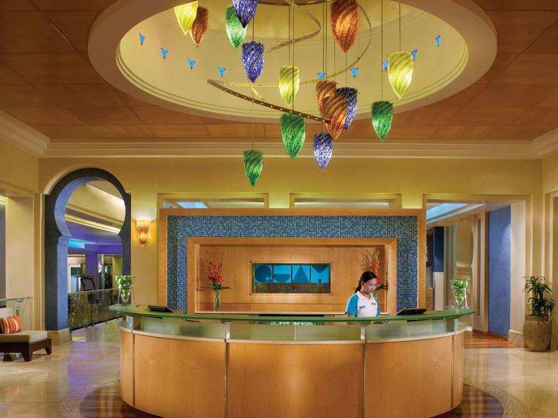 Hotelová recepce s kulatým pultem a barevnými závěsnými lampami.