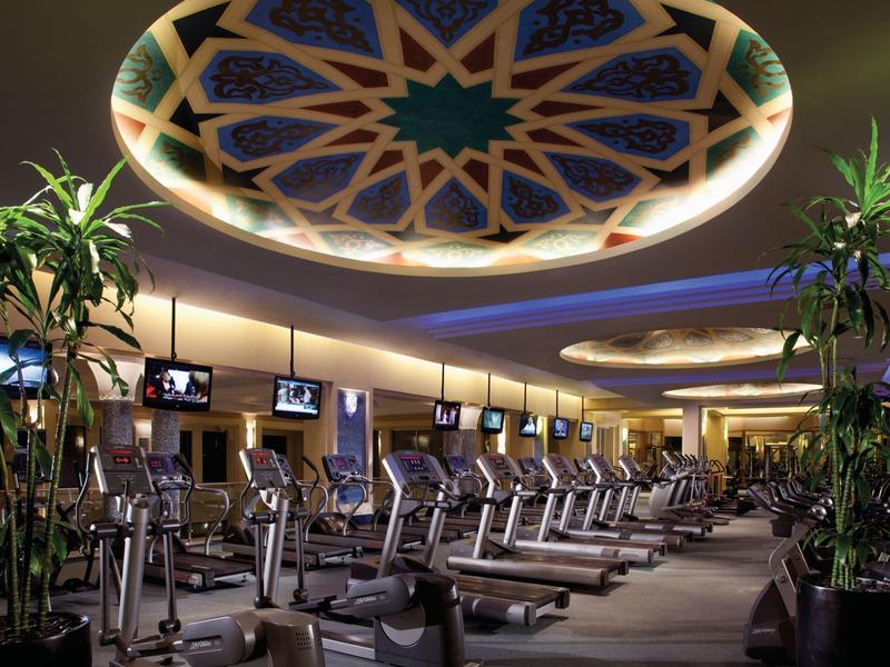Moderní posilovna s běžeckými pásy a dekorativním osvětleným stropem v hotelu.