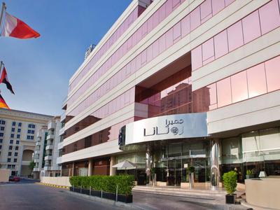 Modernes Hotelgebäude mit gläserner Fassade und Fahnen davor bei klarem Himmel.