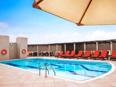 Moderner Außenpool mit roten Liegen und Sonnenschirm auf einer Hotelterrasse