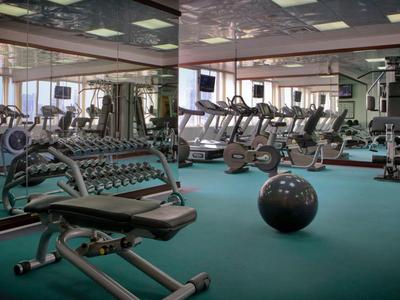 Prostorná posilovna s různým tréninkovým vybavením a velkými zrcadly na stěnách.