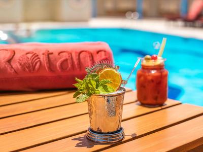 Cocktails und ein rotes Handtuch auf einem Holztisch neben einem blauen Pool.