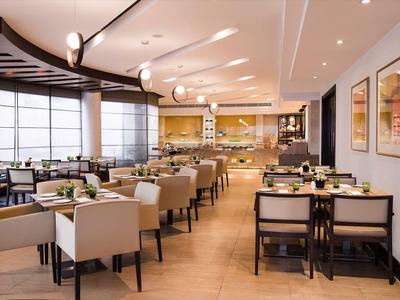 Moderner Restaurantbereich mit hellen Möbeln, großen Fenstern und gedeckten Tischen.