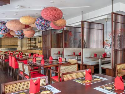 Modernes Restaurant mit roten Stühlen, Holztischen und bunten Lampions an der Decke.