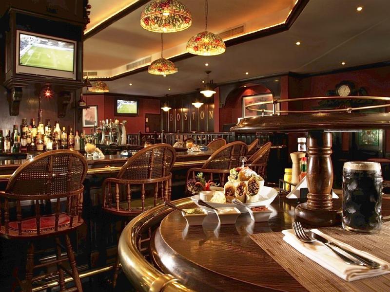 Příjemný hotelový bar s dřevěným nábytkem, pultem a několika televizory na zdi.