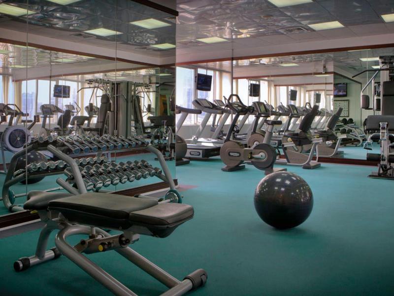 Prostorná posilovna s různým tréninkovým vybavením a velkými zrcadly na stěnách.