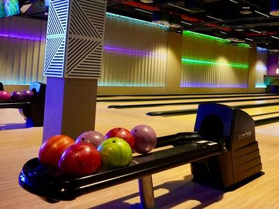 Innenansicht einer Bowlingbahn mit mehreren bunten Bowlingkugeln auf einer Ablage.