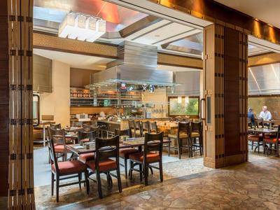 Moderní hotelová restaurace s dřevěným nábytkem a otevřenou kuchyní.