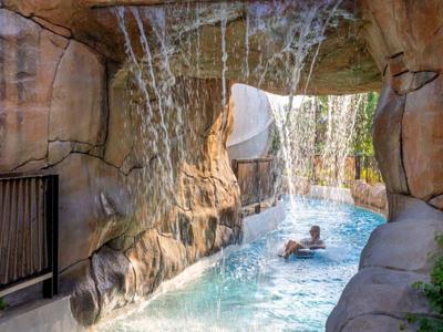 Osoba relaxuje v bazénu s vodopádem v skalním jeskynním prostředí.