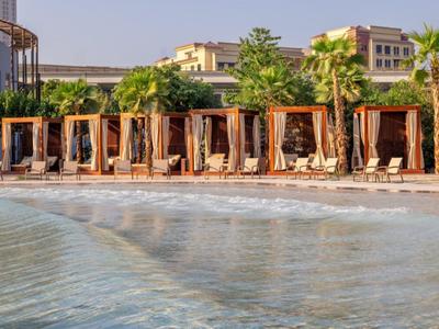 Pláž s dřevěnými kabinami a lehátky před vícepodlažními budovami při východu slunce.