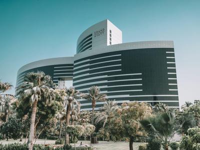 Moderní zakřivená budova hotelu s palmami a jasnou oblohou v pozadí.