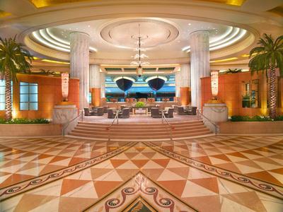 Elegantní hotelová hala s kolonádami, tropickými rostlinami a geometrickou mramorovou podlahou.